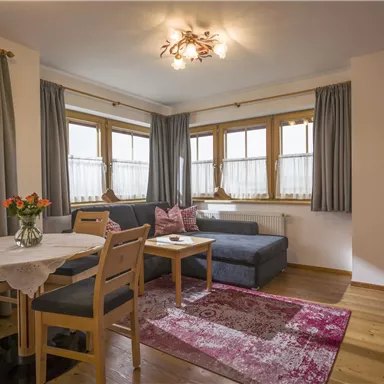 Ein gemütliches Wohnzimmer mit einem Couchbereich und einem Esstisch. Große Fenster lassen viel Licht herein und die Einrichtung ist modern und einladend.