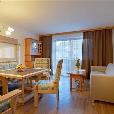 A cozy living space with a dining area and a sofa. Large windows provide plenty of daylight.