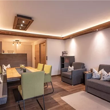 A modern living room with a large dining area. The decor is cozy and stylish, featuring a mix of gray and green furniture.