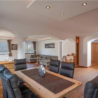 Ein helles und modernes Wohnzimmer mit einem großen Esstisch und eleganten Stühlen. Der Raum ist gut beleuchtet und hat eine gemütliche Atmosphäre.