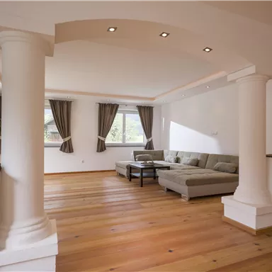 Ein modernes Wohnzimmer mit einem eleganten Sofa und großen Fenstern. Die Wände sind hell und die Holzfußböden verleihen eine warme Atmosphäre.