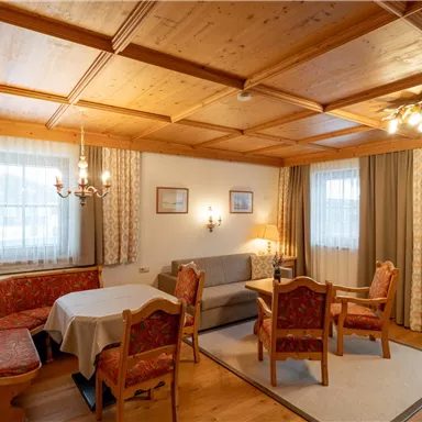 Ein gemütlicher Wohnraum mit einem Holztisch und mehreren Stühlen. Die Wände sind mit Holz vertäfelt, und große Fenster sorgen für viel Licht.