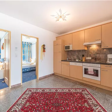 A bright kitchen with modern appliances and a red carpet. In the background, there are two doors leading to bedrooms.