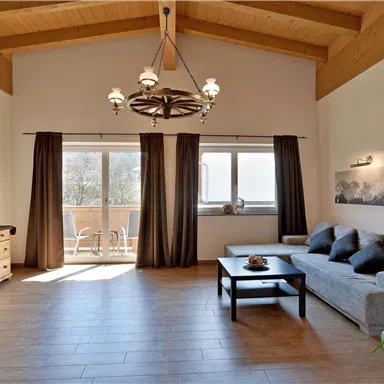 Ein heller Wohnraum mit hohen Decken und Holzdetails. Im Vordergrund befindet sich ein Sofa und ein Couchtisch, neben einem großen Fenster mit Blick nach draußen.