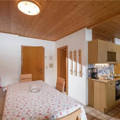 A cozy living kitchen with a dining table and wood paneling. The kitchen is modernly equipped and there is plenty of light in the room.
