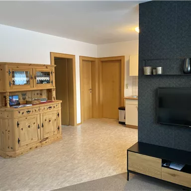 Ein gemütlicher Wohnraum mit einem Holzschrank und einem Fernseher. Zu sehen sind helle Wände und zwei Türen, die in andere Räume führen.