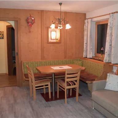 Ein gemütlicher Wohnraum mit Holzverkleidung, einem Esstisch und einer Eckbank. Die Beleuchtung schafft eine entspannte Atmosphäre.