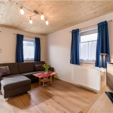 A cozy living space with a modern sofa and a table. Large windows with blue curtains let in plenty of light.