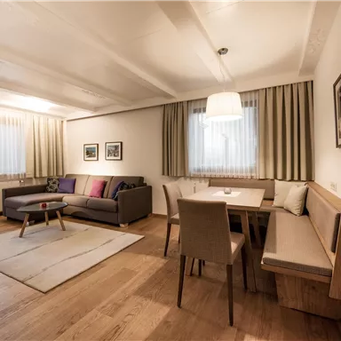 A modern living room with a cozy sofa, a dining table, and large windows. The room is bright and welcoming, with hardwood flooring and pretty decor.