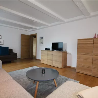 A modern living room with a gray sofa and a round table. Pictures hang on the wall, and a TV is on a wooden cabinet.