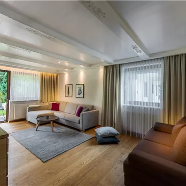 A modern living room with two sofas, a coffee table, and a television. Large windows provide plenty of natural light and a view of the outdoors.