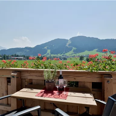 Ein schöner Blick von einer Terrasse auf grüne Wiesen und Berge. Auf dem Tisch stehen zwei Gläser und eine Flasche Wein.