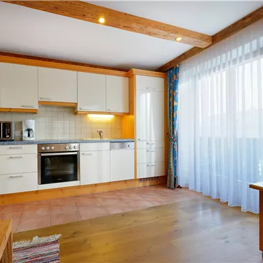 Eine moderne Küche mit hellen Schränken und einem großen Fenster. Der Raum ist gemütlich und gut beleuchtet.