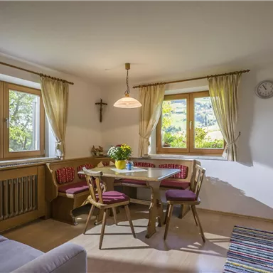 Eine gemütliche Küche mit einem runden Tisch und Stühlen. Licht durchflutet den Raum durch die großen Fenster.