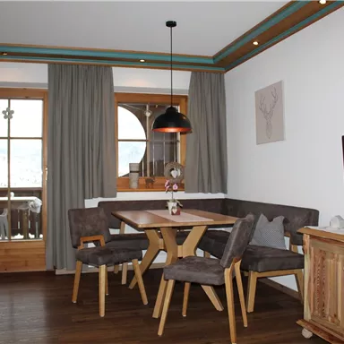 Ein gemütlicher Essbereich mit einem Holztisch und Stühlen. Große Fenster bieten Blick nach draußen und lassen viel Licht herein.