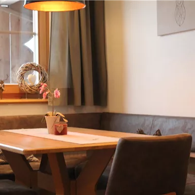 Ein gemütlicher Essbereich mit einem Holztisch und einer Bank. An der Wand hängt ein dekoratives Element und eine Blume steht als Tischschmuck.