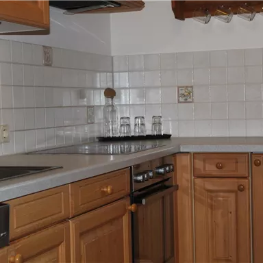 Eine helle Küche mit Holzschränken und weißen Fliesen. Sie ist ausgestattet mit einem Herd, einem Waschbecken und einer Mikrowelle.