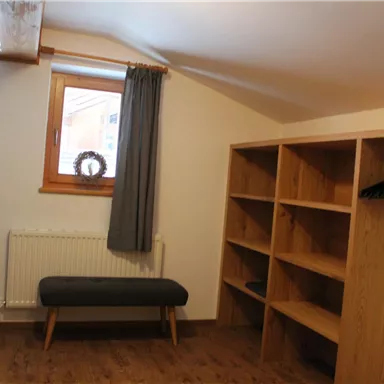 Ein gemütlicher Raum mit einem Fenster, einem kleinen Holzsofa und Regalen. Der Boden ist aus Holz und der Raum ist hell und einladend.