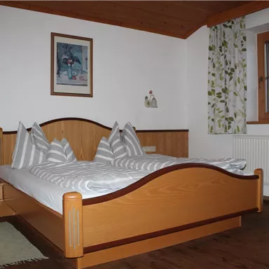 Ein gemütliches Schlafzimmer mit einem Doppelbett und hellem Holz. Die Wände sind mit floralem Vorhang und einem Kunstwerk dekoriert.