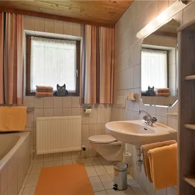 A bright bathroom with a bathtub and a sink. Towels in warm colors are neatly stacked and windows provide natural light.