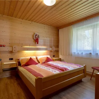 A cozy bedroom with wooden paneling and two beds. Large windows provide plenty of daylight.