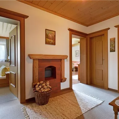 An inviting hallway with wooden elements and a fireplace. On the left, a door leads to a bright room with windows.