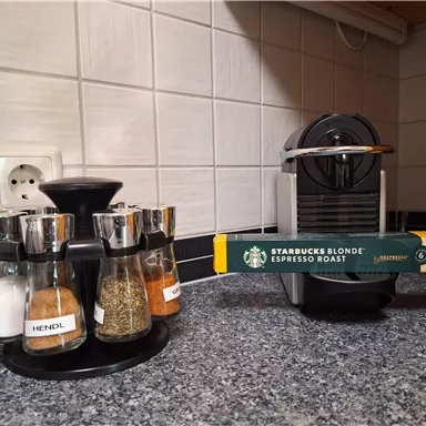 A modern kitchen with a coffee machine and a spice rack. The spice rack contains various spices and is situated on a gray countertop.