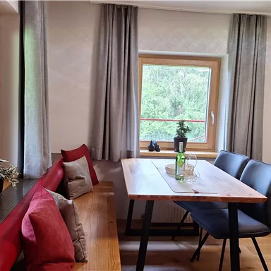 A cozy dining area with a wooden table and black chairs. Large windows provide a beautiful view of the green nature outside.