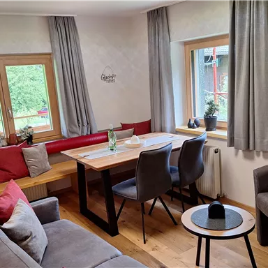 A cozy living space with a dining table and chairs. Large windows let in plenty of daylight and offer a view of nature.