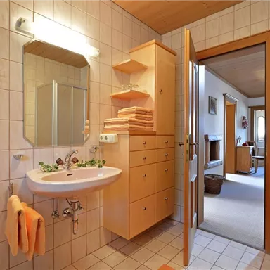 A modern bathroom with bright tiles and a sink. In the background, a cozy room with furniture is visible.