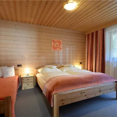 A cozy bedroom with wooden paneling. It contains a double bed and a single bed, as well as large windows that let in plenty of light.