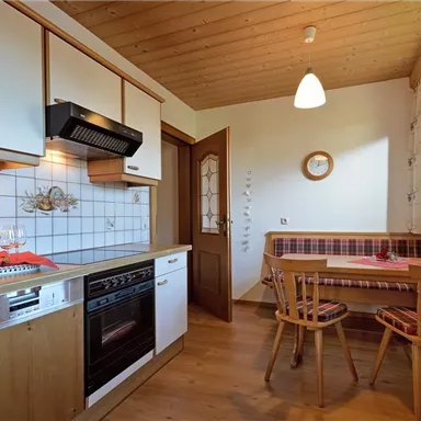 A modern kitchen with wood details and bright colors. There are chairs at the table and a bottle of wine, along with plenty of natural light.