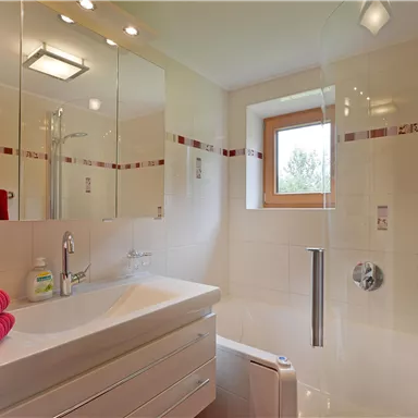 A modern bathroom with a sink and mirrors. Red towels are neatly placed on the shelf.