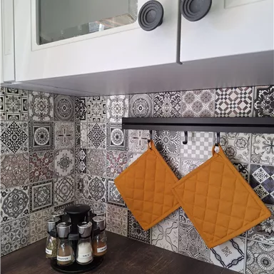 A modern kitchen with a colorful tiled backsplash. Two orange pot holders hang on a hook above a spice rack.