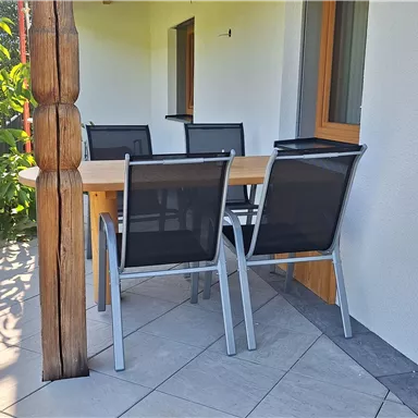 An outdoor dining area with a table and black chairs. The surroundings are bright and inviting, ideal for relaxed meals.