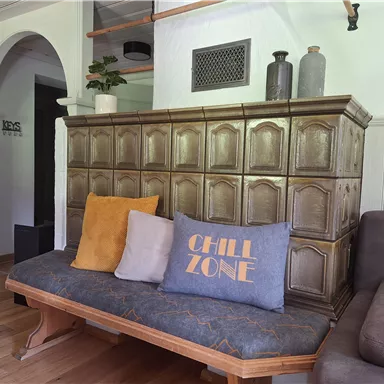 A cozy living area with a wooden bench, decorative cushions, and a stylish tiled stove. The furnishings exude a relaxed atmosphere.