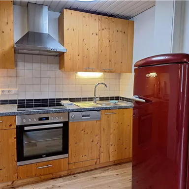 A modern kitchen with wooden cabinets and stainless steel appliances. A red refrigerator stands next to the countertop.