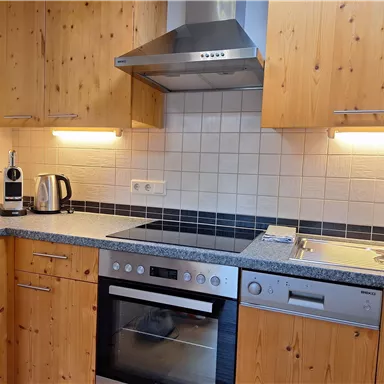 A modern kitchen with wooden cabinets and a gray work area. The equipment includes a stove, a kettle, and a sink.