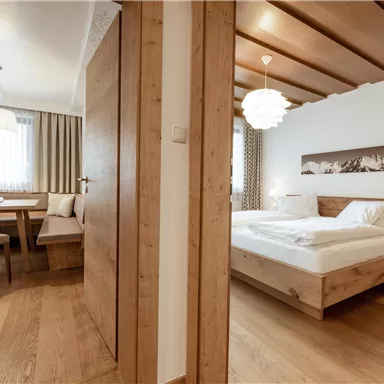 A modern room with wooden furniture and a cozy atmosphere. There is a dining table, chairs, and a large window that lets in plenty of light.