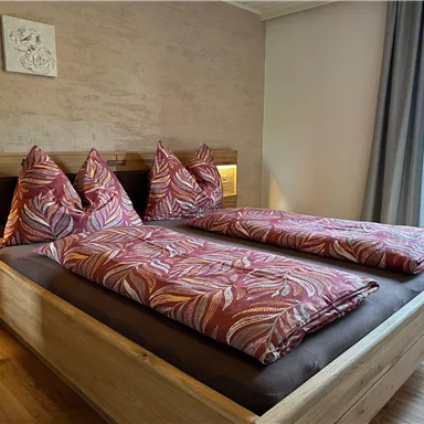A cozy bedroom with a double bed and colorful cushions. There are windows overlooking a balcony and warm wood paneling.