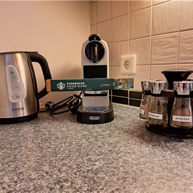 A kitchen counter with a kettle, a coffee machine, and a spice rack. On the coffee machine, there is a pack of Starbucks house blend.