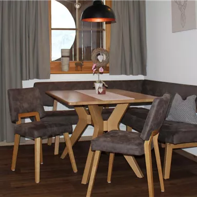 Ein gemütlicher Wohnraum mit einem Essbereich, einem Holztisch und bequemen Stühlen. Große Fenster bieten Blick auf die Umgebung und sorgen für natürliches Licht.