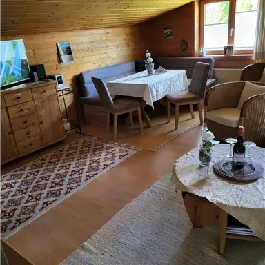 A cozy room with wooden walls and a large window. There is a dining area with a table and chairs as well as a relaxed seating area.