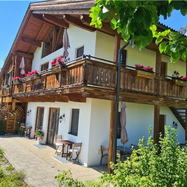 Ein gemütliches Holzhaus mit einem Balkon, geschmückt mit Blumen. Umgeben von grünem Gras und Bäumen, strahlt es eine einladende Atmosphäre aus.