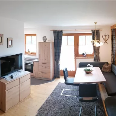 Ein gemütlicher Wohnraum mit Holzverkleidung, einem Esstisch und einer Couch. Der Raum verfügt über große Fenster, die viel Licht hereinlassen.