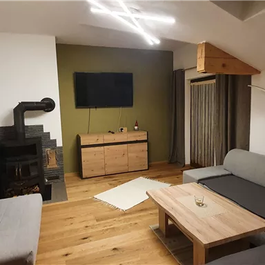 A modern living room with gray sofas and a wooden floor. The room is bright and cozy, with a TV and a decorative fireplace.