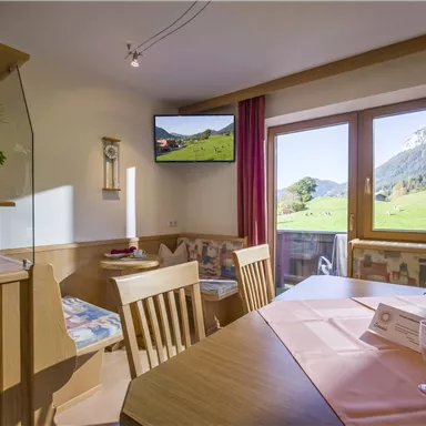 A cozy apartment with a dining area and large windows offering a view of the green landscape. A TV and decorative elements create an inviting atmosphere.