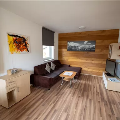 Ein modernes Wohnzimmer mit einer gemütlichen Couch, einem Couchtisch und einem Fernseher. An der Wand hängen Kunstwerke und es gibt einen Holzakzent.