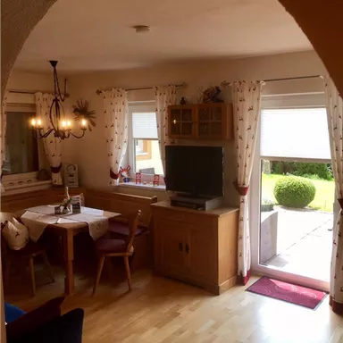 Ein gemütlicher Wohnraum mit einem Essbereich und einem Fernseher. Großen Fenstern ermöglichen einen Blick auf den Garten.