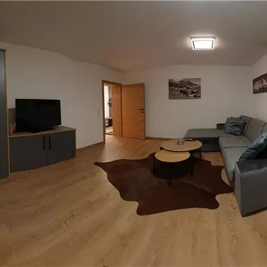 A modern living room with a gray sofa and a coffee table. The room has wooden flooring and neutral walls, with art on the wall.